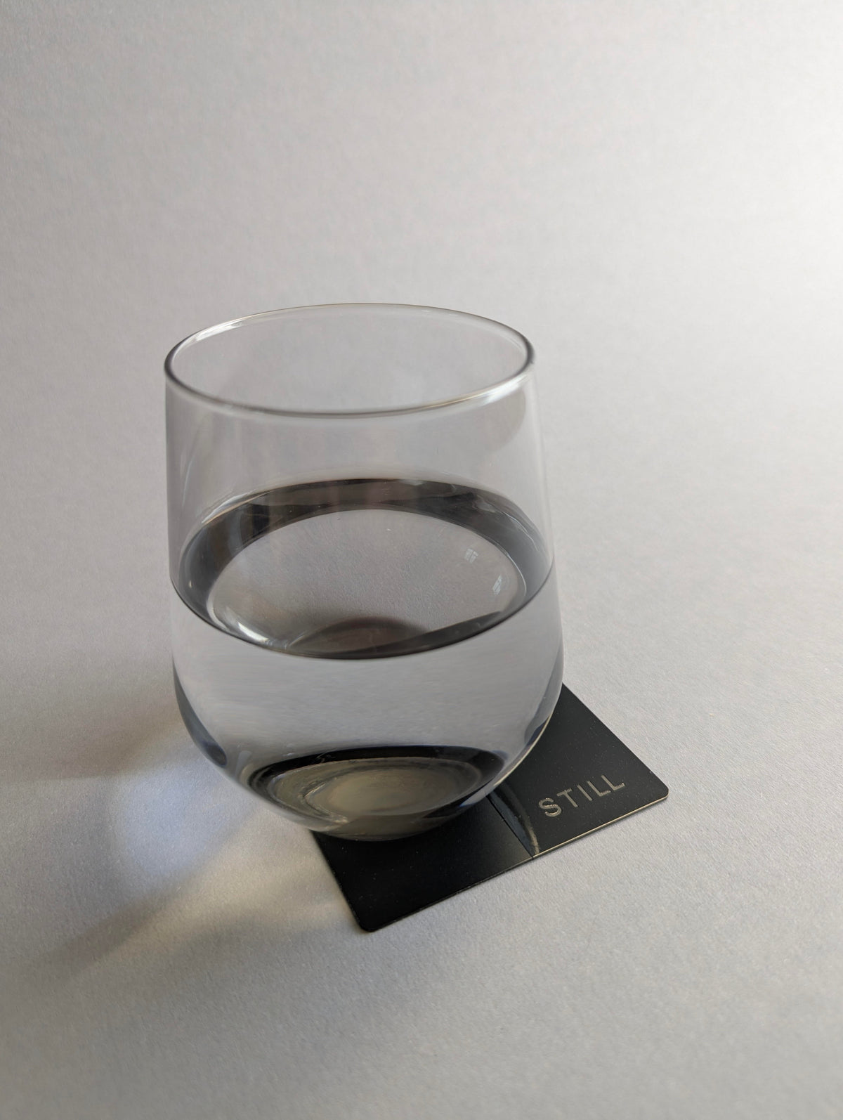 Wasserglas auf der schwarzen STILL-Karte von ELVAR vor einem hellgrauen Hintergrund.